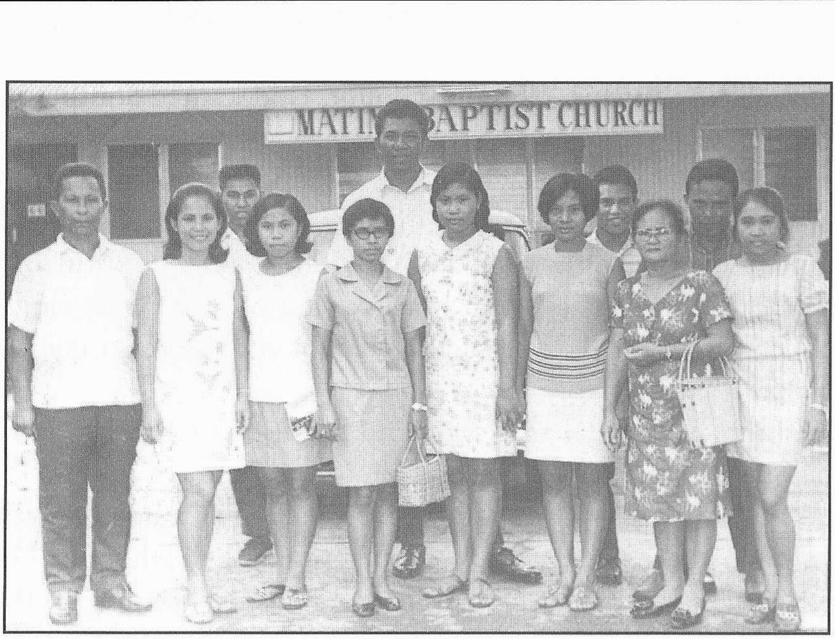 Thirteen men and women standing in front of the Matina Baptist Church sign.
